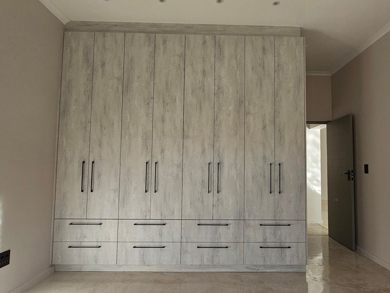 A spacious bedroom featuring extensive floor-to-ceiling built-in cupboards with a modern wood-grain finish, recessed lighting, and polished tiled flooring.