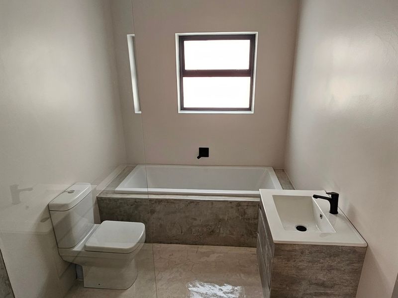Modern bathroom featuring a built-in bathtub, vanity with basin, toilet, and contemporary black tapware with neutral tiled finishes.