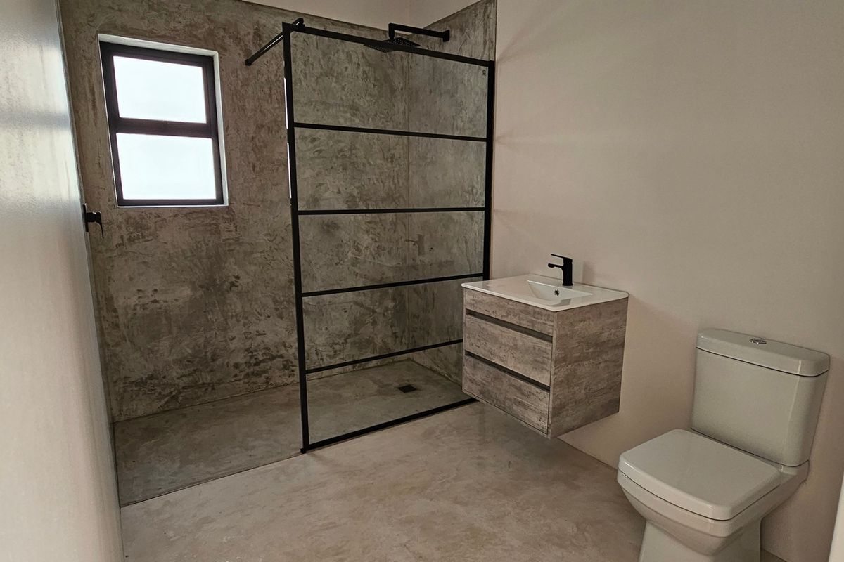 Modern bathroom featuring a walk-in shower with a black-framed glass screen, wall-mounted vanity, and contemporary cement-look wall finishes.