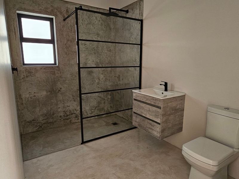 Modern bathroom featuring a walk-in shower with a black-framed glass screen, wall-mounted vanity, and contemporary cement-look wall finishes.