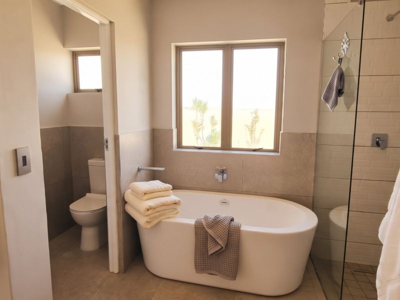 Modern bathroom featuring a freestanding bathtub, separate glass-enclosed shower, and neutral tiled finishes, providing a clean and functional space.