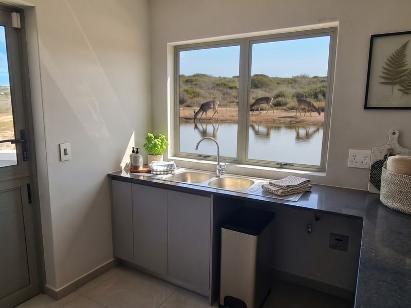 A modern scullery featuring a double bowl sink, stone countertops, and built-in cabinetry, with a large window offering scenic views of the surrounding landscape.