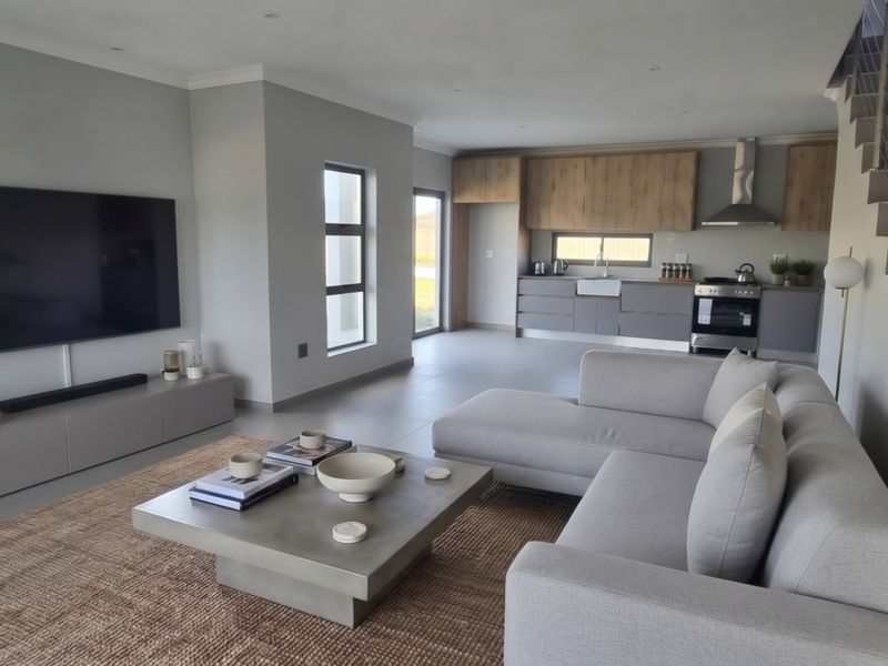 Modern open-plan living area featuring a contemporary kitchen with wood-tone cabinetry, farmhouse sink, and a sleek staircase leading to the upper level.