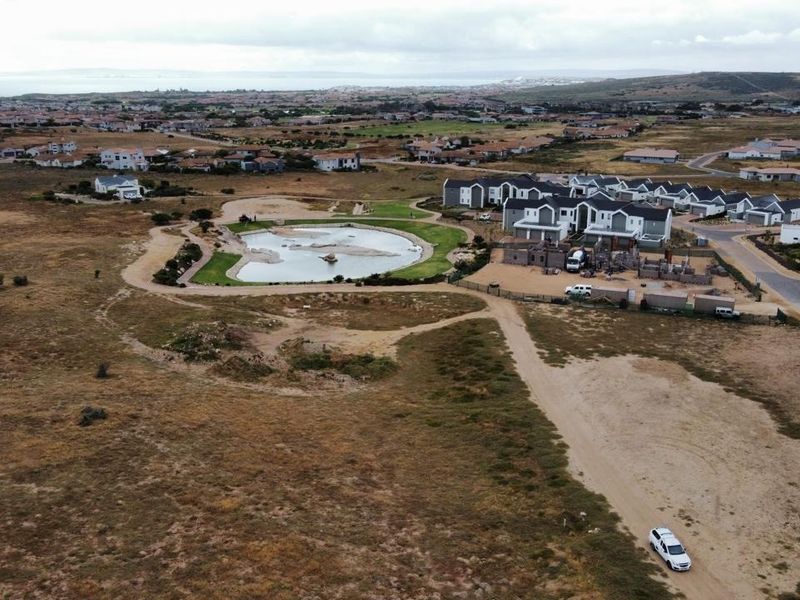 Aerial view of a residential estate development featuring a central pond and surrounding landscape in a coastal setting.