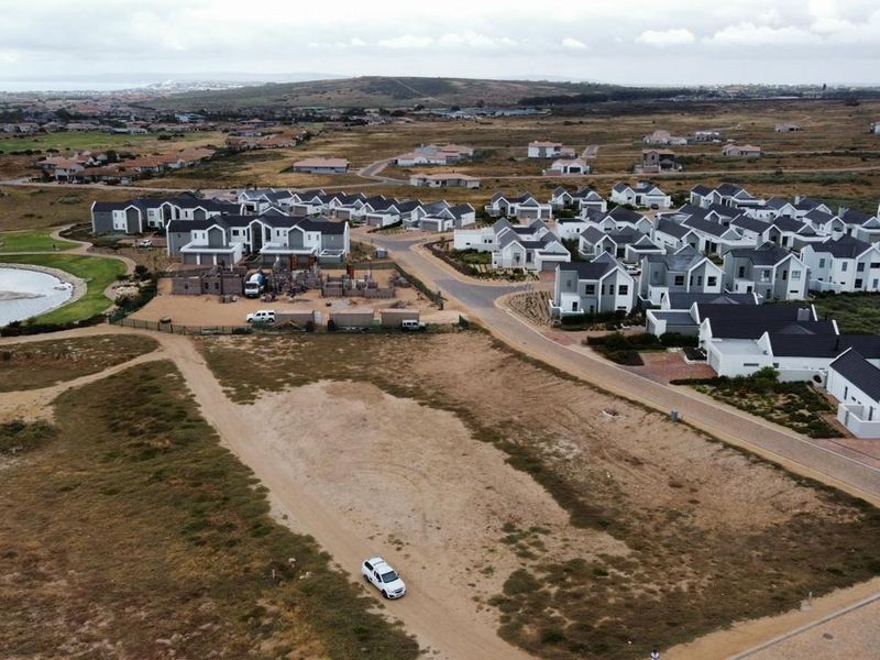 An aerial view of a modern residential housing estate featuring paved roads, uniform architectural styles, and a nearby stormwater pond.