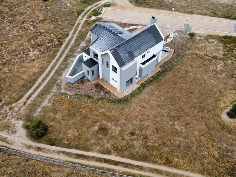 Aerial view of a modern detached house featuring a tiled roof with solar panels, a chimney, and surrounding landscaped grounds.