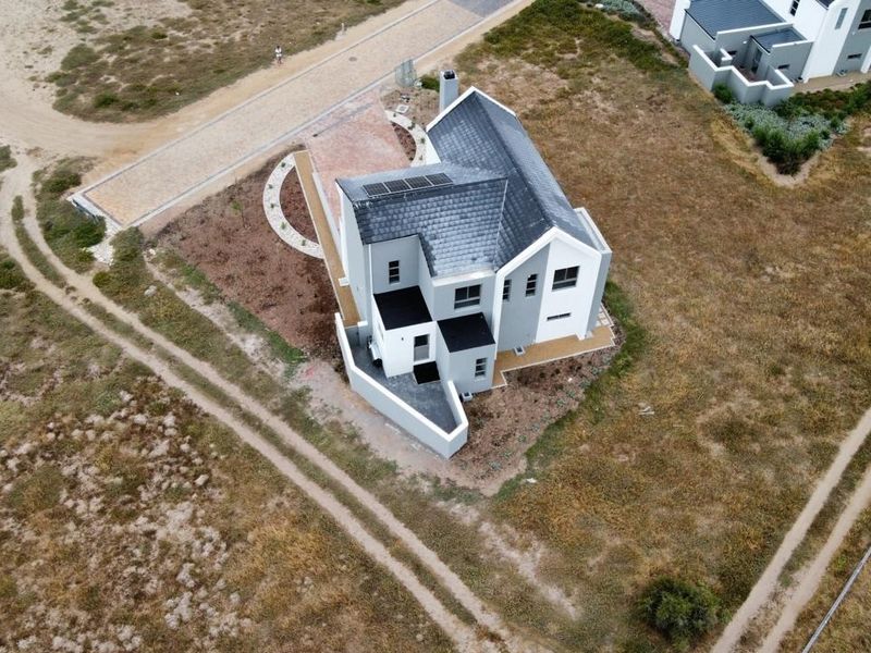 Aerial view of a modern residential property featuring a tiled roof with solar panels, a paved driveway, and surrounding landscaped grounds.