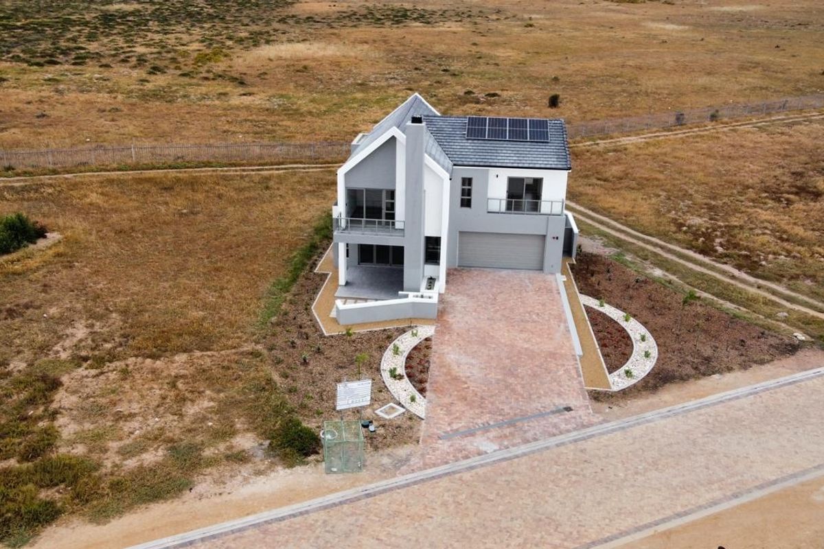 Aerial view of a modern two-story house featuring a paved driveway, double garage, solar panels, and a balcony, set in a spacious landscape.