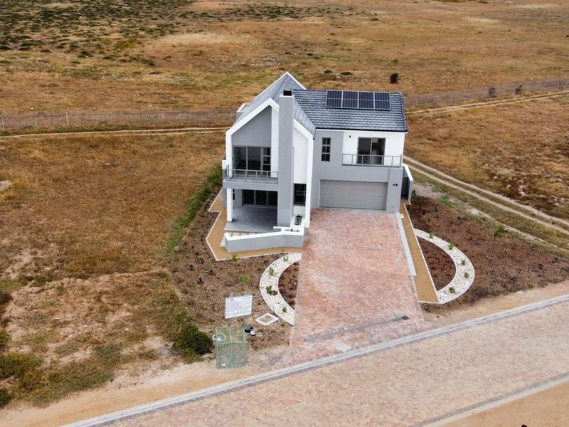 Aerial view of a modern two-story house featuring a paved driveway, double garage, solar panels, and a balcony, set in a spacious landscape.
