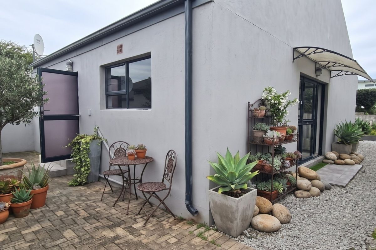 A well-maintained rear exterior area featuring paved patio space, gravel landscaping, and modern aluminium window frames with a protective awning.