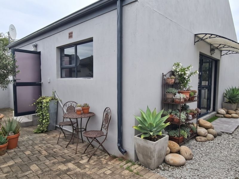 A well-maintained rear exterior area featuring paved patio space, gravel landscaping, and modern aluminium window frames with a protective awning.
