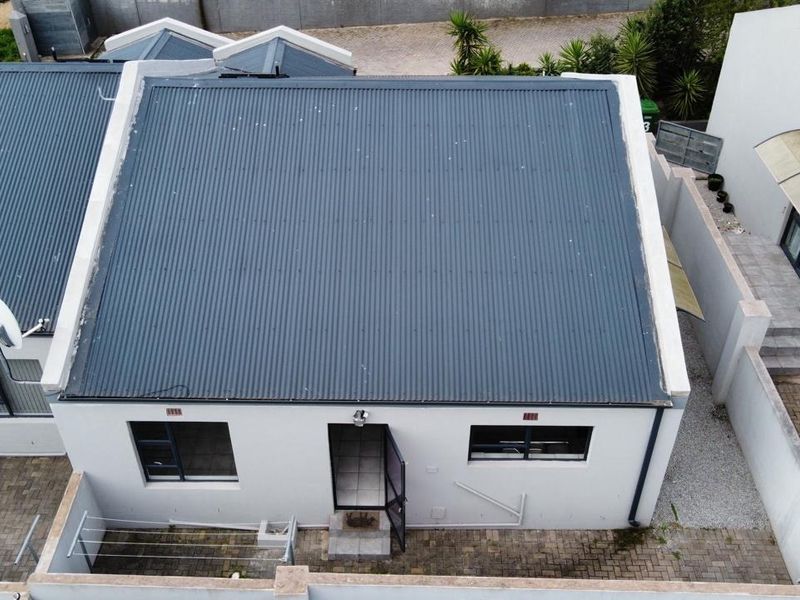Aerial view of a residential property featuring a corrugated metal roof, paved driveway, and secure entrance.