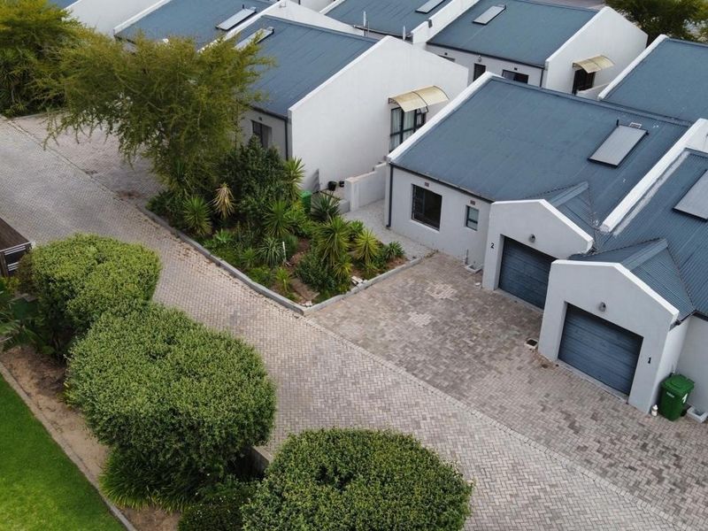 Aerial view of a residential complex featuring paved driveways, garages, and well-maintained metal roofs with integrated solar water heating panels.