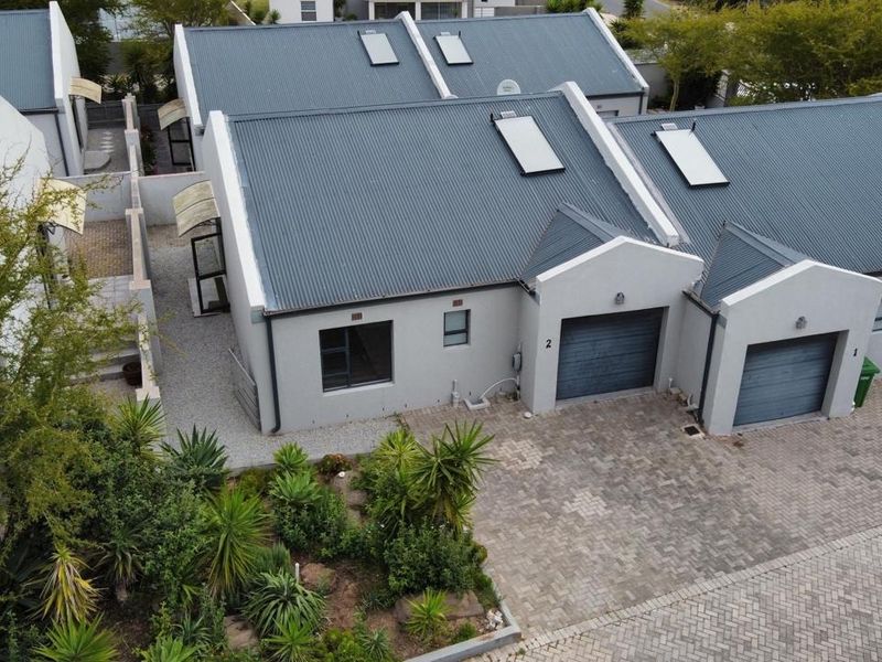 Aerial view of a residential complex featuring corrugated metal roofs, skylights, paved driveways, and well-maintained landscaped garden areas.
