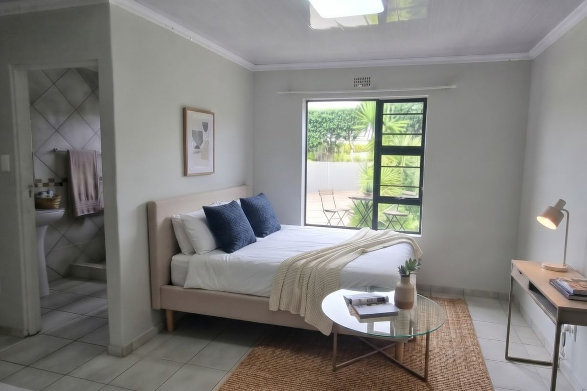 A well-lit bedroom featuring tiled flooring, a coved ceiling, and an adjoining en-suite bathroom with a pedestal basin, overlooking a private outdoor area.