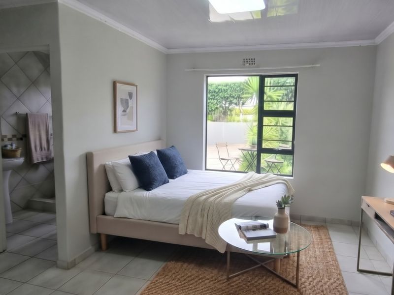 A well-lit bedroom featuring tiled flooring, a coved ceiling, and an adjoining en-suite bathroom with a pedestal basin, overlooking a private outdoor area.