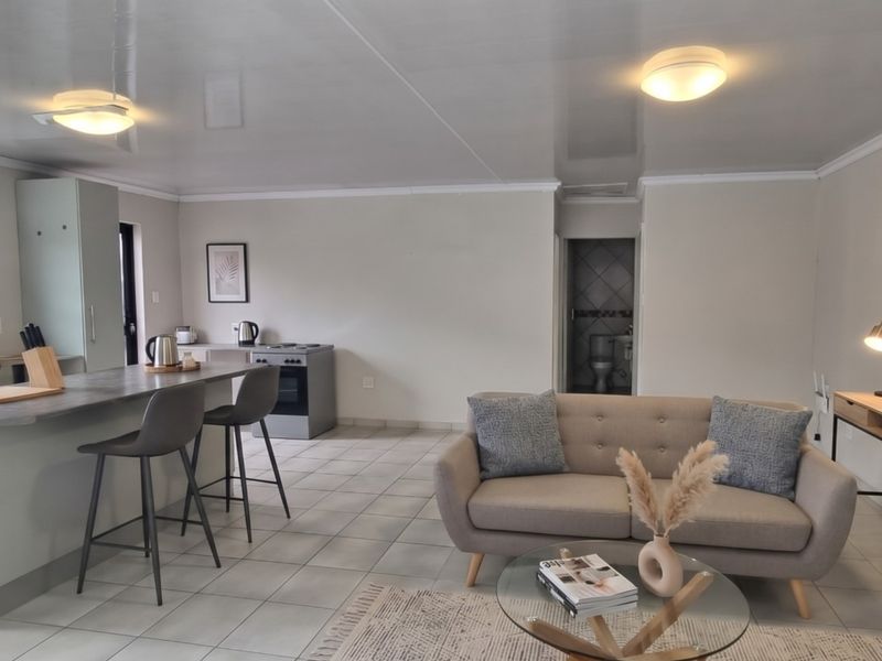 An open-plan living and kitchen area featuring tiled flooring, a central kitchen island with breakfast bar seating, and a functional kitchen layout.
