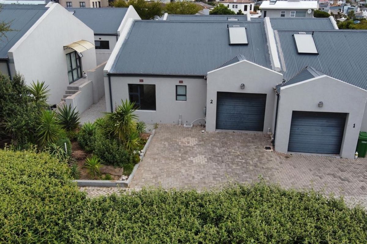 Aerial view of a residential property featuring a paved driveway, garage access, and modern corrugated metal roofing with integrated skylights.
