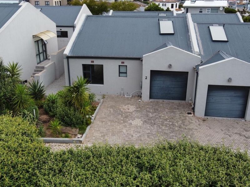 Aerial view of a residential property featuring a paved driveway, garage access, and modern corrugated metal roofing with integrated skylights.