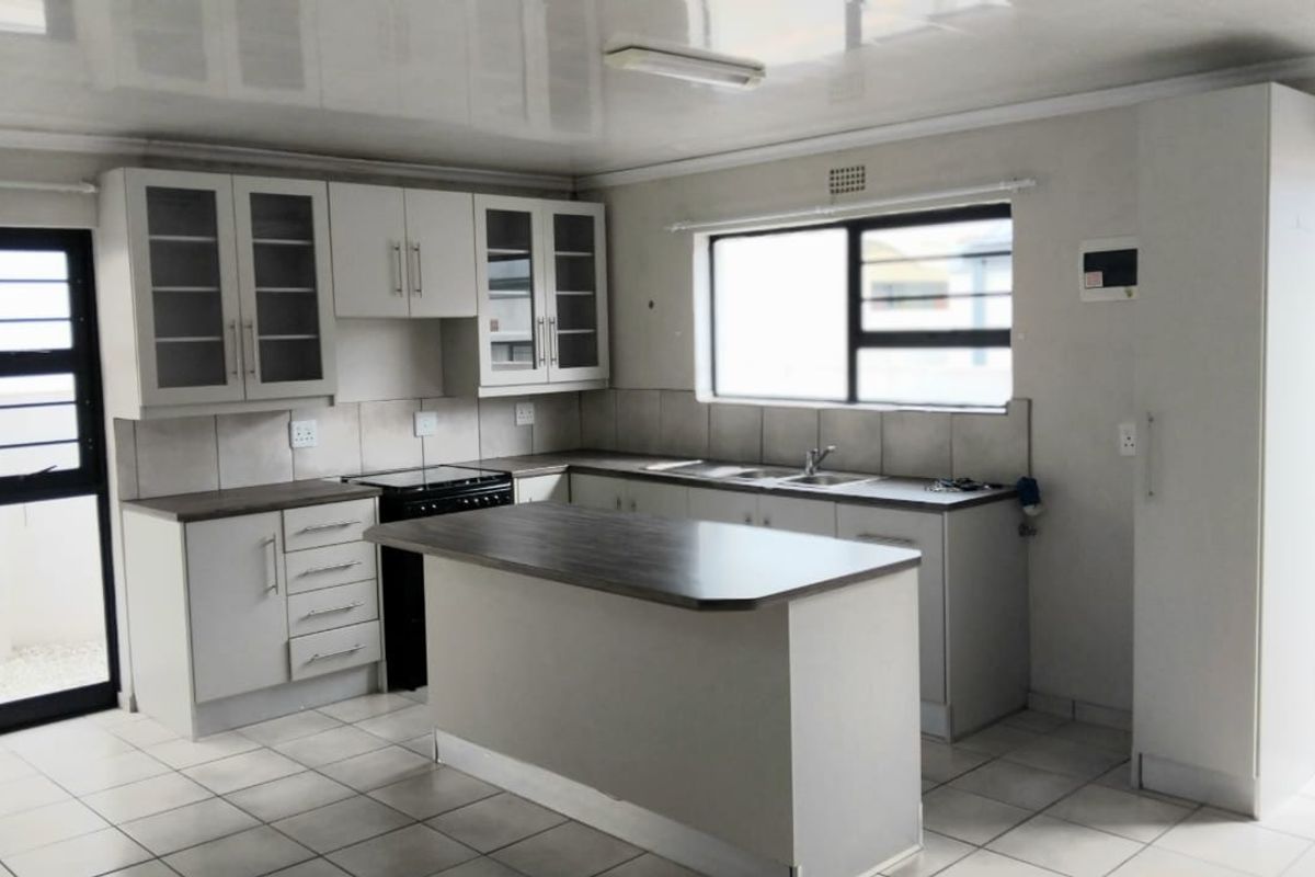 A clean, functional kitchen featuring white cabinetry, a central island, tiled flooring, and a double sink with ample natural light.