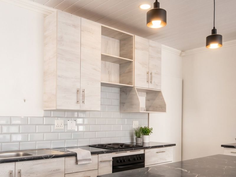 Modern kitchen featuring light wood-grain cabinetry, subway tile backsplash, dark stone countertops, and integrated appliances with stylish pendant lighting.