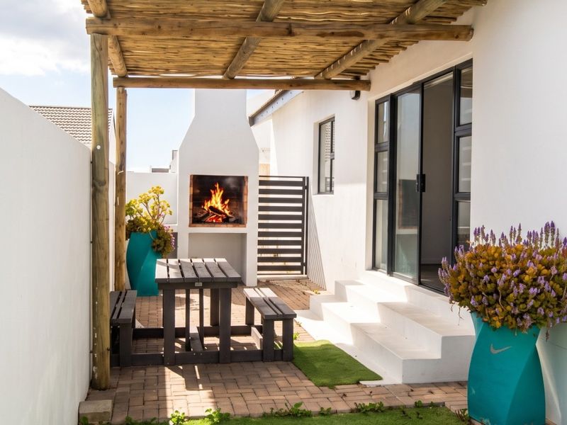 A well-maintained outdoor patio featuring a built-in braai, timber pergola, and paved flooring, providing a functional space for outdoor entertaining.