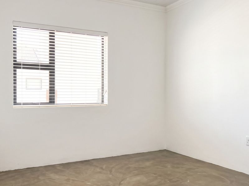 A bright, empty bedroom featuring polished concrete flooring, built-in cupboard storage, and venetian blinds on the window.