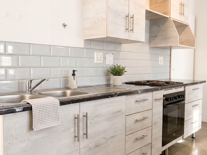 Modern kitchen featuring light wood-grain cabinetry, subway tile backsplash, stainless steel sink, and integrated oven with electric hob.