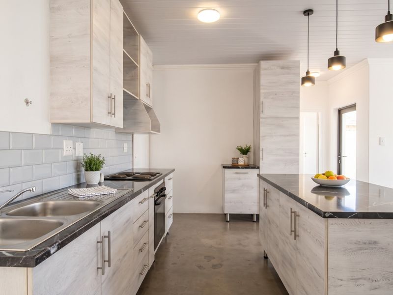 Modern kitchen featuring light wood-grain cabinetry, stone countertops, a central island, subway tile backsplash, and sleek pendant lighting over a polished concrete floor.