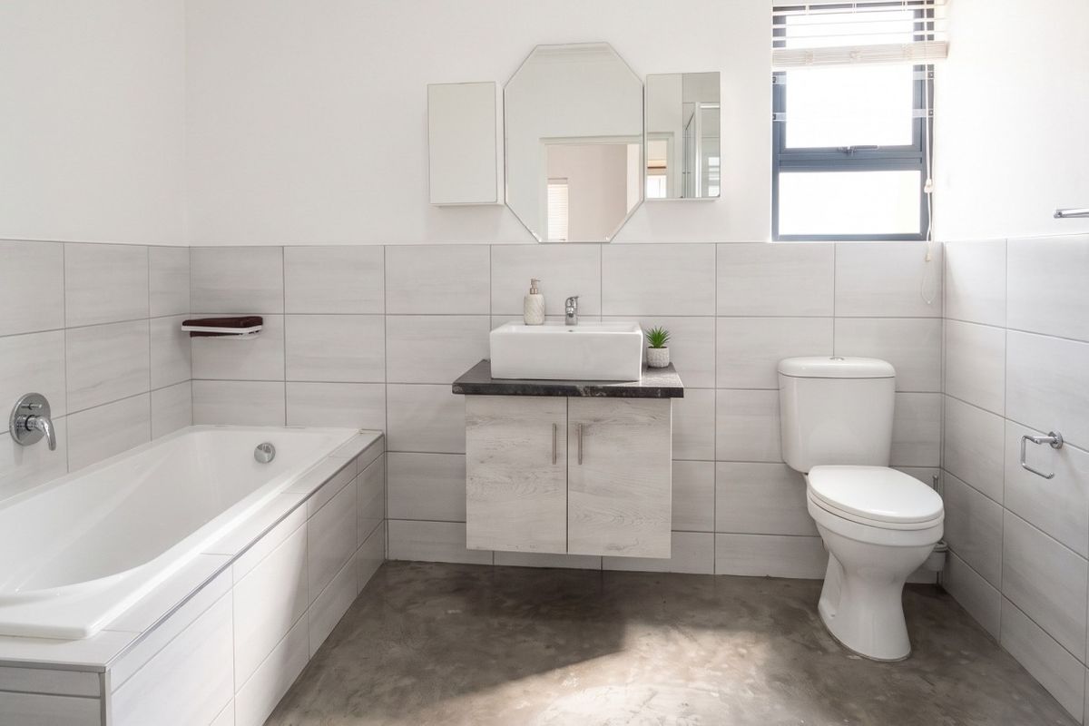 A modern bathroom featuring a built-in bathtub, wall-mounted vanity with vessel sink, toilet, and neutral tiled walls, offering a clean and functional space.