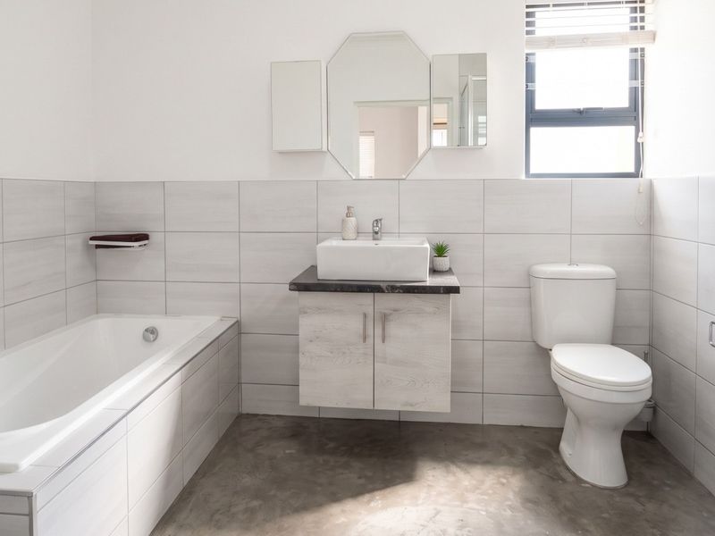A modern bathroom featuring a built-in bathtub, wall-mounted vanity with vessel sink, toilet, and neutral tiled walls, offering a clean and functional space.