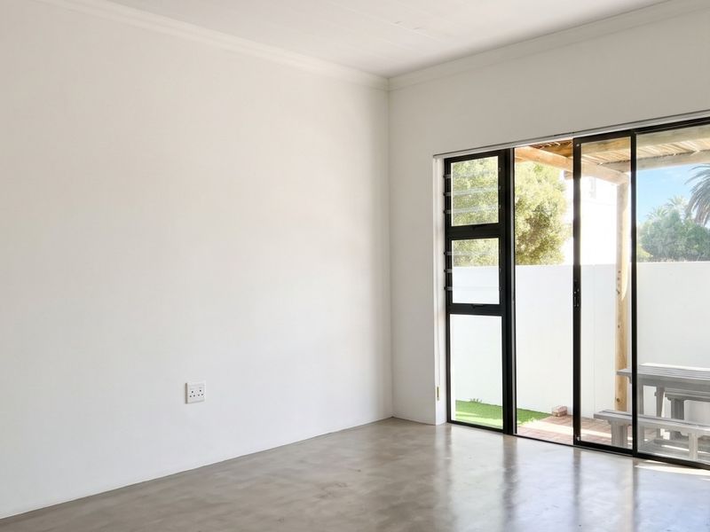 A bright, empty living room featuring polished concrete floors and large sliding glass doors that open onto an outdoor patio area.