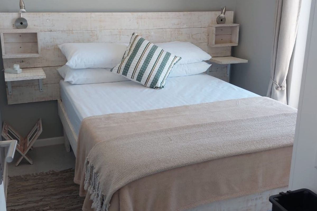 A cozy bedroom featuring a custom built-in wooden headboard with integrated bedside shelving and wall-mounted reading lights.