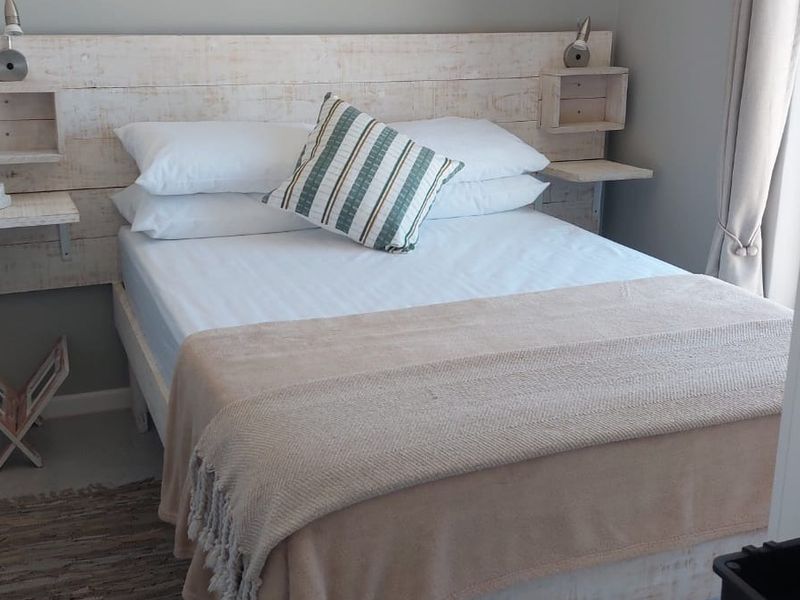 A cozy bedroom featuring a custom built-in wooden headboard with integrated bedside shelving and wall-mounted reading lights.