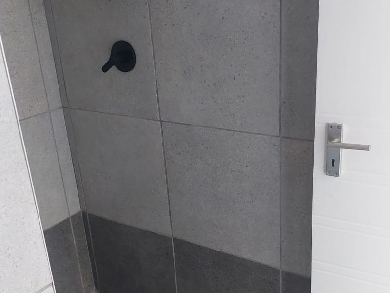 A modern bathroom shower area featuring contemporary grey wall tiles and a matte black shower mixer.