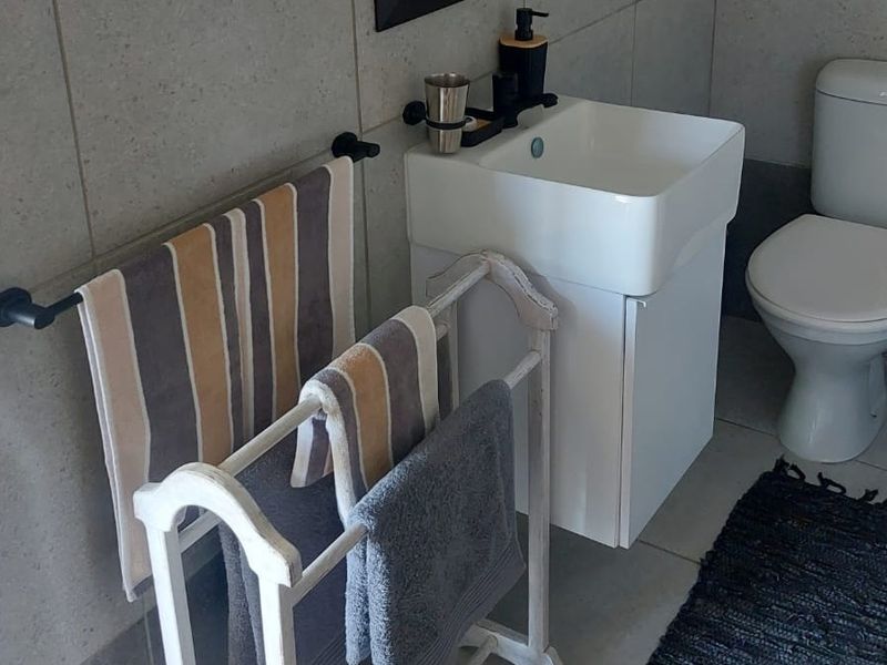 A compact, modern bathroom featuring a wall-mounted vanity with a ceramic basin, a standard toilet, and neutral wall and floor tiling.