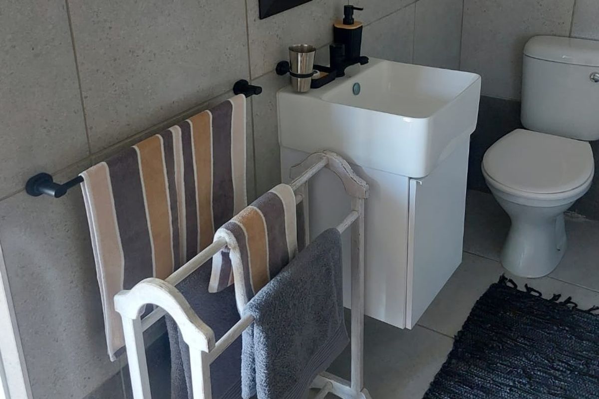 A compact, modern bathroom featuring a wall-mounted vanity with a ceramic basin, a standard toilet, and neutral wall and floor tiling.