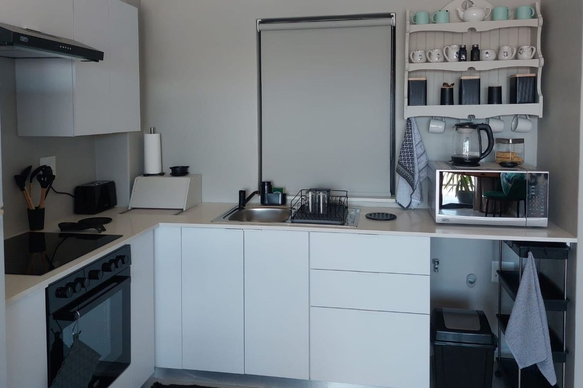 A modern, compact kitchen featuring white cabinetry, stone countertops, a built-in oven, electric hob, and a stainless steel sink.