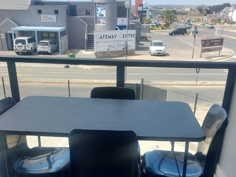 A balcony area featuring a metal balustrade and tiled flooring, offering an elevated view of the surrounding commercial street and parking area.