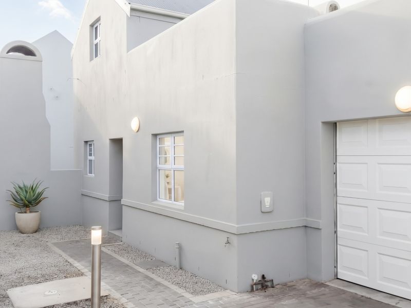 Front exterior view of the townhouse featuring a garage, paved walkway, gravel garden area, and modern neutral facade finishes.