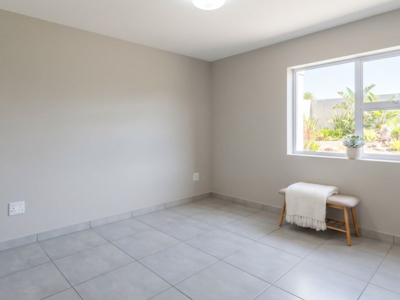 A bright, neutral-toned bedroom featuring large windows, tiled flooring, and clean finishes, offering a versatile space ready for personalization.