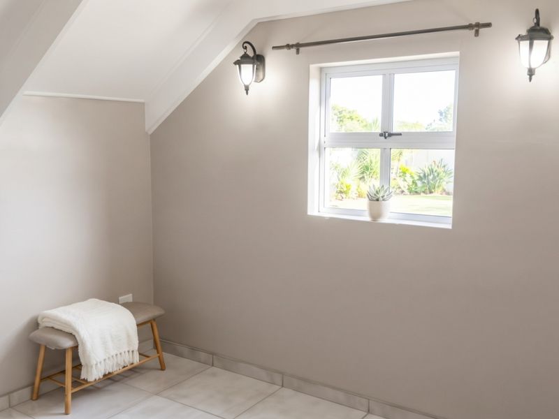 A bright, neutral-toned bedroom featuring sloped ceilings, tiled flooring, and wall-mounted lighting, offering a clean and versatile space.