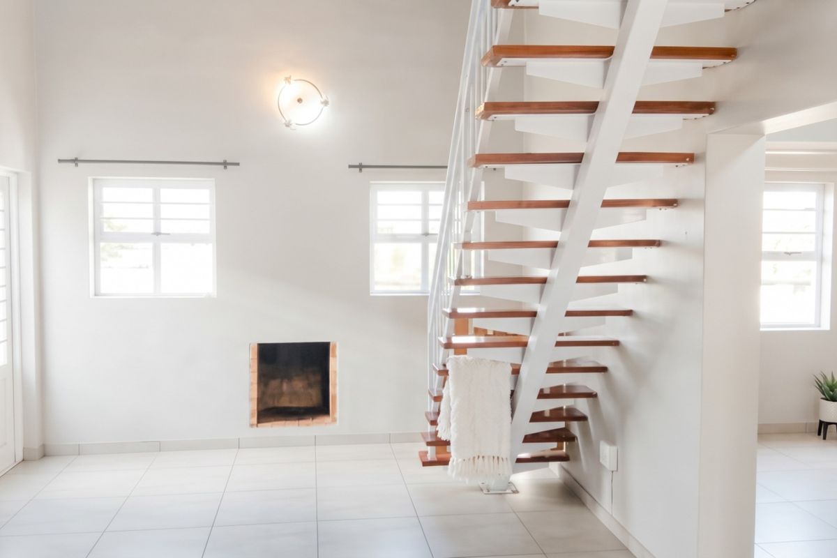 Bright and airy living area featuring an open-tread staircase, built-in fireplace, and neutral tiled flooring throughout.
