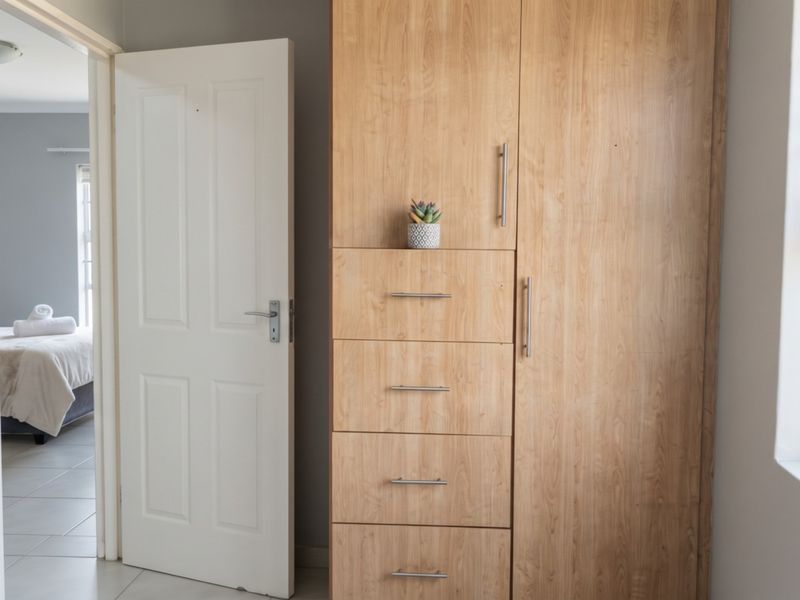 A bedroom featuring a light wood built-in wardrobe, tiled flooring, and a view into an adjacent room.