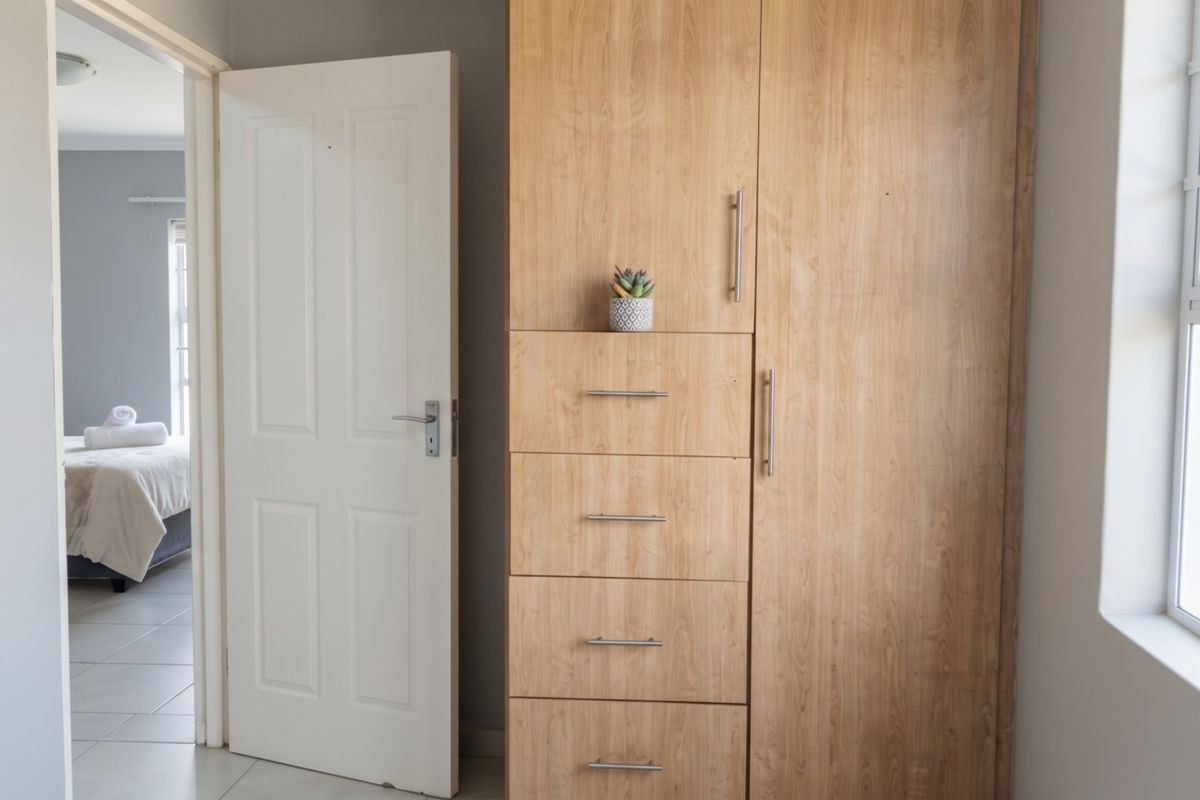 A bedroom featuring a light wood built-in wardrobe, tiled flooring, and a view into an adjacent room.