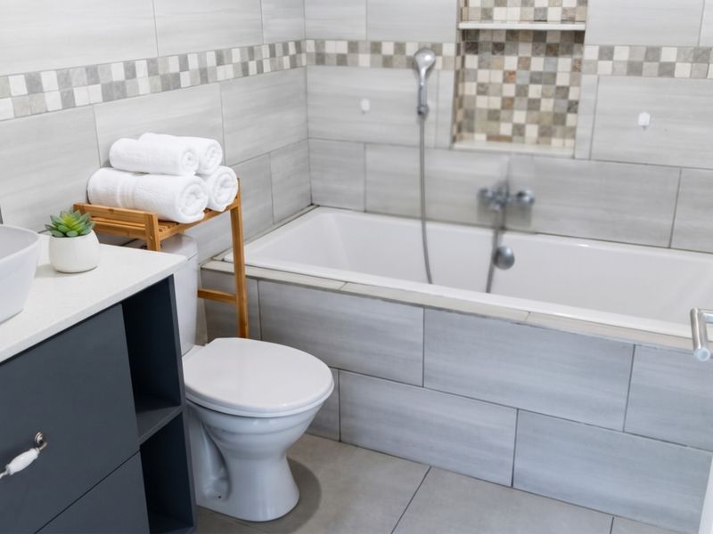 Modern bathroom featuring a built-in bathtub with a recessed niche, a vanity cabinet with a countertop basin, and neutral tiled finishes.