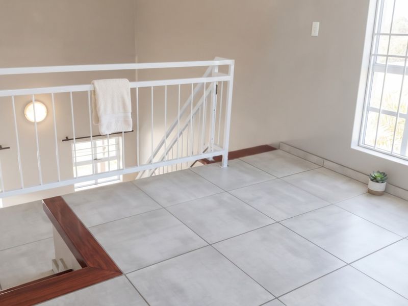 A bright and spacious landing area featuring modern tiled flooring, a white metal balustrade, and large windows with security bars.