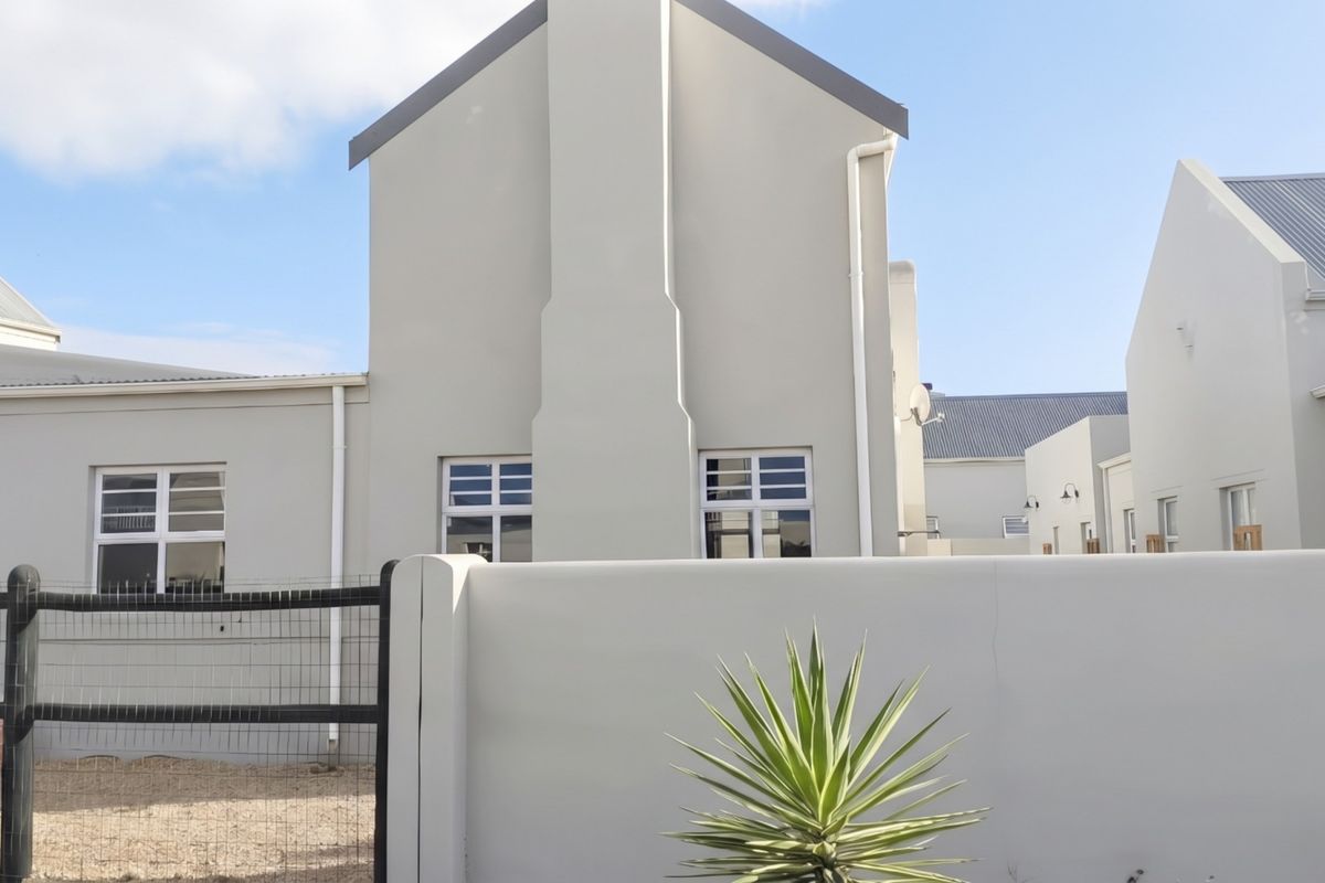 A view of the rear exterior of the townhouse featuring a gabled roof, external chimney stack, and a secure boundary wall with fencing.
