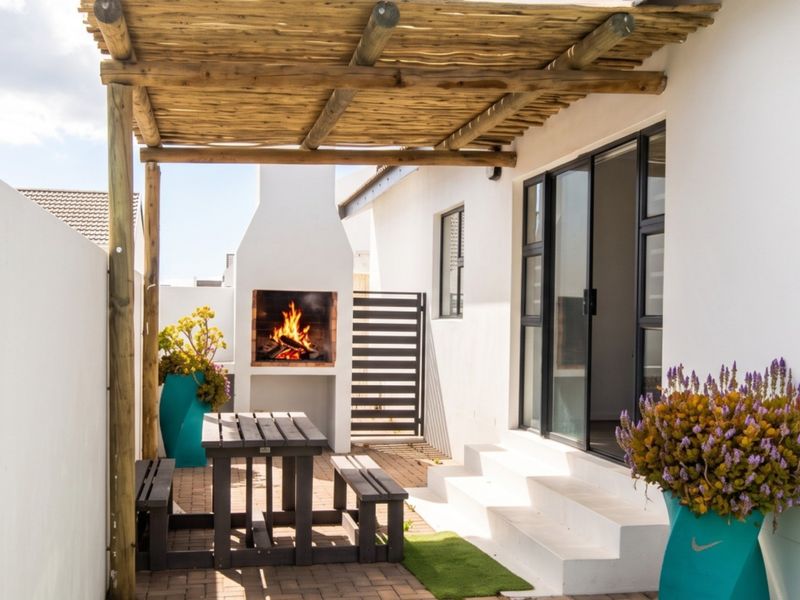 A covered outdoor patio featuring a built-in braai, timber pergola, and direct access to the interior through sliding glass doors.