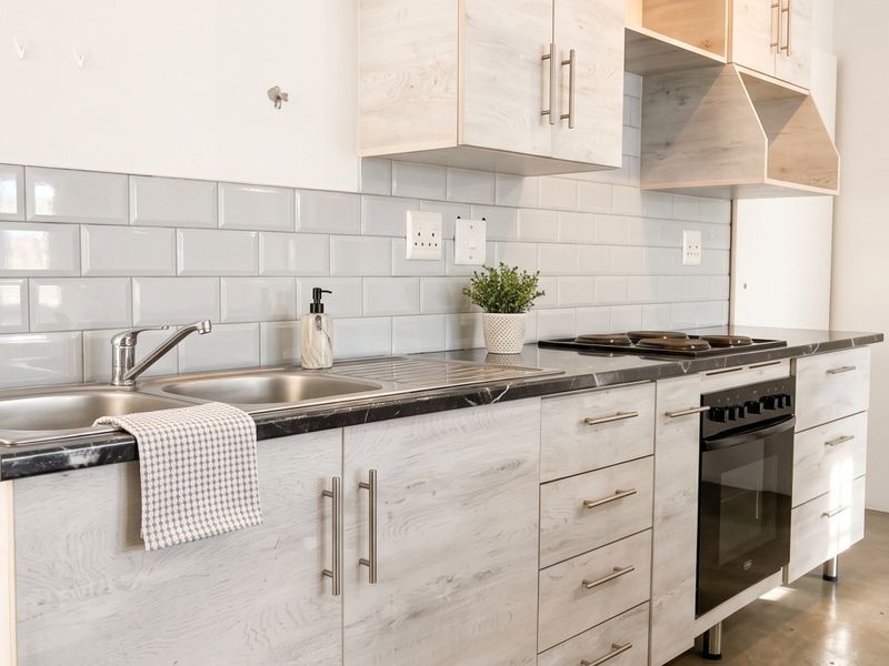 A modern kitchen featuring light wood-grain cabinetry, a marble-effect countertop, subway tile backsplash, and integrated stainless steel appliances.